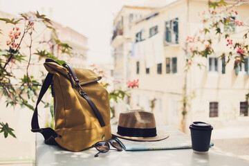Travel items on cafe table with beautiful italian street at background. Hat, backpack, sunglasses,...