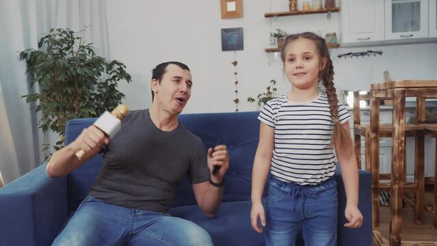 dad and daughter a sing dancing at home. stay home active leisure parents with children happy childhood dream concept. dad and daughter dancing sing next to the sofa with a microphone. kid dance