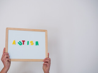 White board with the word autism, on a white background, held by hands. Health concept.