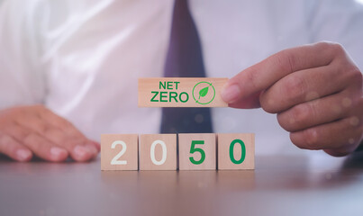 Hand puts wooden cubes with net zero icon in 2050 on grey background. Net zero by 2050. Carbon...