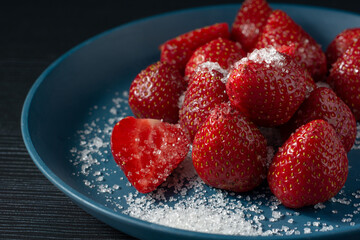 Strawberries on a plate with dark background. Strawberries on a plate with a sprinkle of sugar.