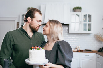 Pastry chef confectioner young caucasian woman with husband love boyfriend man try taste of cake on kitchen home table. Cakes cupcakes and sweet dessert