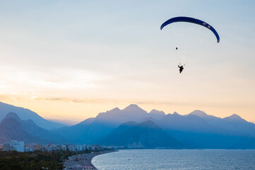 Silhouette of a man on a paraglider flying over the sea at sunset.