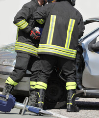 two uniformed firefighters use a powerful hydraulic shear to open a passenger car after the accident
