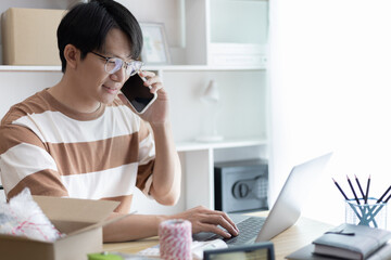 Asian man is taking online orders from a phone and chatting with customers to confirm their order, Selling products online or doing freelance work at home, Working at home and owning businesses.