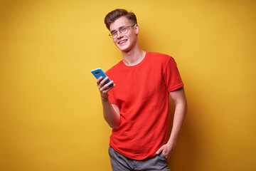 Youth and technology. Young handsome man using smartphone against yellow background.