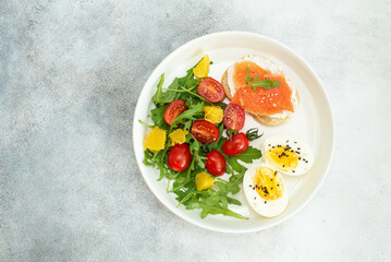 salad with tomatoes, two salmon sandwiches, boiled egg on the white plate, top view