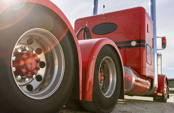 Classic red American semi truck in parking lot, detail of aluminum tandem axles with red hub caps. Low angle, rear view of big rig. Wide angle of powerful diesel US lorry. 