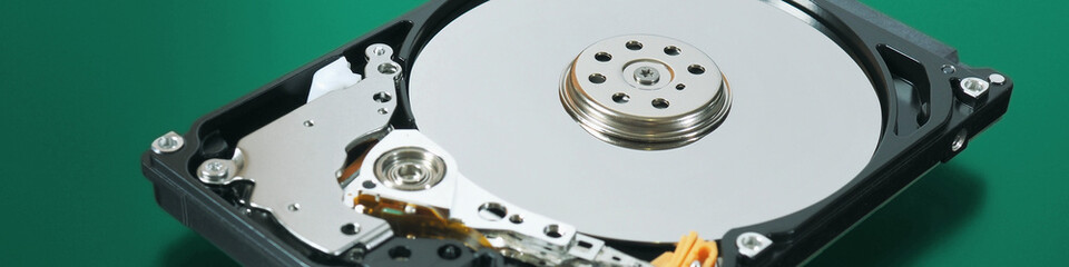 A disassembled open hard disk drive HDD of a computer or laptop lies on a green matte surface. IT closeup. Banner about computer hardware and equipment. Data storage headline. Macro