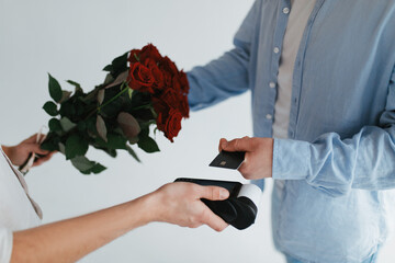 A young millenial man buys red roses for his girlfriend with a credit card for Valentine's day.
