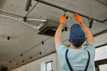 Male electrician fixing ceiling lamp in building