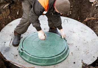 The worker closes the manhole cover of the sewer well. Installation of a septic tank in a country house