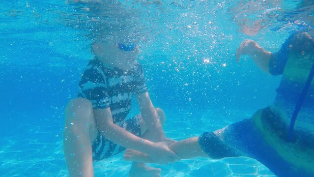 Child enjoying summer vacation. Underwater view of happy toddler boy diving into swimming pool and smiling