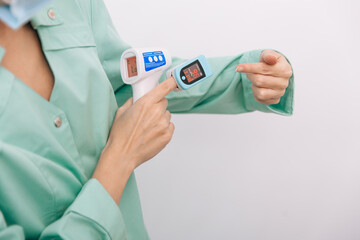 Temperature measurement gun in doctor hands. Close-up shot of doctor wearing protective surgical mask ready to use infrared isometric thermometer gun to check body temperature for virus symptoms