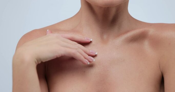 Close-up beauty portrait of young woman with smooth and healthy skin strokes her skin at collarbone area against gray background. Skin care.