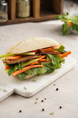 Traditional vietnamese banh mi sandwich with sliced smoked tofu, fresh spinach, shredded carrots and peeled cucumbers, cilantro on marble board on light grey textured background