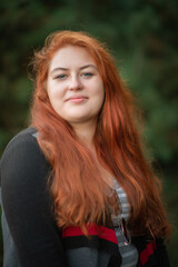 Naklejka premium Portrait of a young beautiful full chubby red-haired girl in the park.