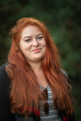 Portrait of a young beautiful full chubby red-haired girl in the park.