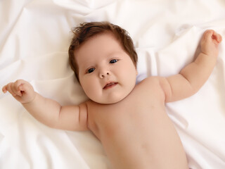 Cute 1 month old Baby girl infant on a bed on her belly with head up looking into camera with her big eyes. Natural bedroom light. Infant baby. Healthy and medical concept. Happy pregnancy childbirth