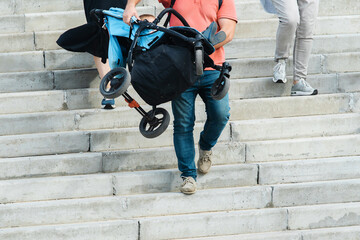The father carries the baby carriage down the stairs. A man descends the concrete steps with a...