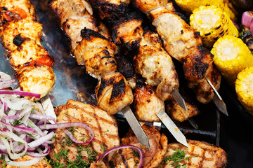 Grilled meat on skewers. Cooking food on fire and coals. Burnt shish kebab pieces garnished with onions and corn. Close-up