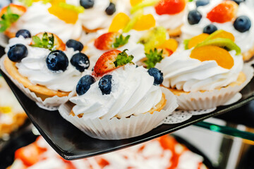 Cakes with cream and berries. Sweet food decorated with strawberries and blueberries is located on the counter in the store. Close-up. selective focus