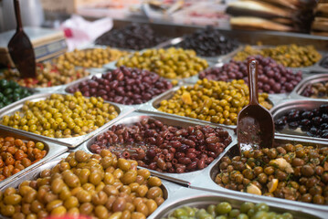 Different colors and taste olives in plastic containers on stall in foreground. Market. Traditional arabic food. Vegetarian. Healthy food, lifestyle. Mediterranean appetizer. 