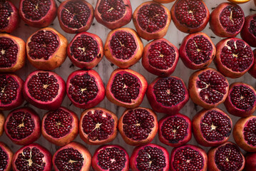 Many red juicy and incised pomegranates liesby lines on table. Wonderful, fresh juice from fruits drinks every day for promote health and replenish body with vitamins. Close-up