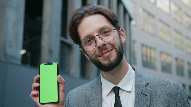 Portrait shot of the handsome smiled caucasian man demonstrating smartphone with green screen and tracking motion. Chroma key concept