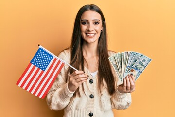 Beautiful brunette young woman holding united states flag and dollars smiling with a happy and cool smile on face. showing teeth.