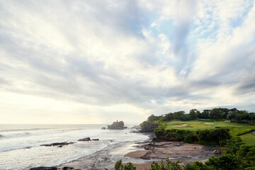 Beautiful balinese landscape. Ocean beach. Ancient hinduism temple Tanah lot on the rock against cloudy sky. Bali Island, Indonesia.