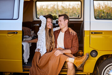 Joyful caucasian couple sitting inside of campervan while looking outside of the van, man and woman have talk, laughing, enjoying summer evening in countryside nature. travel, people lifestyle