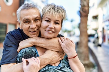 Middle age caucasian couple of husband and wife together on a sunny day outdoors. Smiling happy in love hugging at the city.