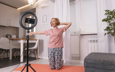 a healthy pensioner sits on the bedroom floor in front of a tripod for a camera, shoots a fitness...