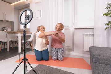 two pensioners are sitting on the bedroom floor in front of a tripod for the camera, shooting a fitness video tutorial for the elderly,