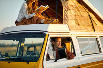 hippie female pretty woman read a book. caravan car vacation. holiday trip in motorhome. beautiful caucasian long haired woman in casual wear reading a book while sitting on top of car trunk.