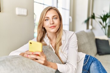 Young blonde woman using smartphone sitting on the sofa at home.