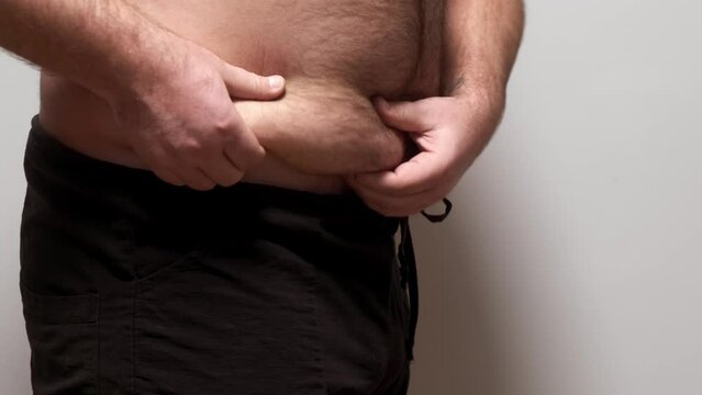 Close-up of a male fat shaking belly on a white background. Obese man touches his belly and is frustrated by being overweight
