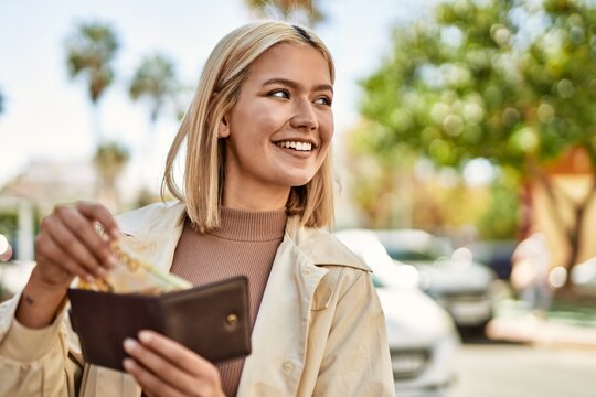 Young blonde girl smiling happy holding wallet with norway krone banknotes at the city.