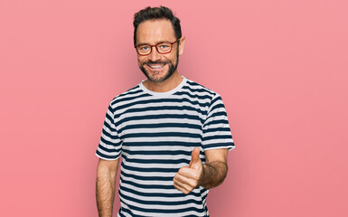Middle age man wearing casual clothes and glasses doing happy thumbs up gesture with hand. approving expression looking at the camera showing success.