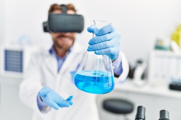 Fototapeta premium Middle age hispanic man wearing scientist uniform using vr glasses holding test tube at laboratory