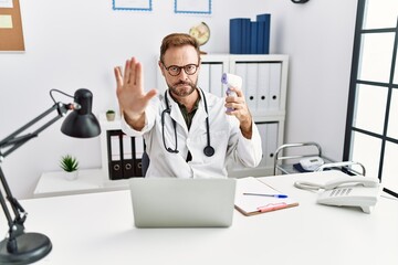 Middle age doctor man holding thermometer at the clinic with open hand doing stop sign with serious and confident expression, defense gesture