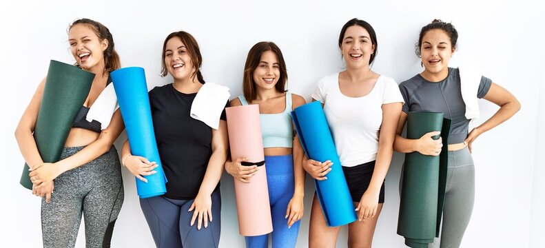 Group of women holding yoga mat standing over isolated background winking looking at the camera with sexy expression, cheerful and happy face.