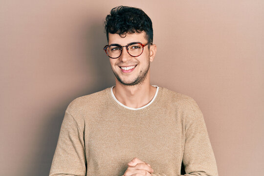 Young hispanic man wearing casual clothes and glasses with hands together and crossed fingers smiling relaxed and cheerful. success and optimistic