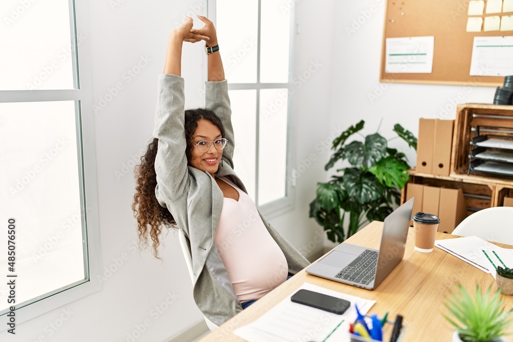 Wall mural Young latin woman pregnant smiling confident stretching arms working at office