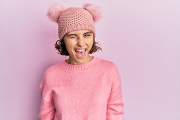 Young brunette woman wearing cute wool cap winking looking at the camera with sexy expression,...