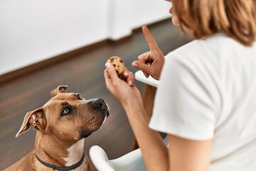 Young caucasian woman teaching dog prohibition eat cookies at home - Powered by Adobe