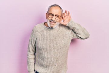 Handsome senior man with beard wearing casual sweater and glasses smiling with hand over ear...
