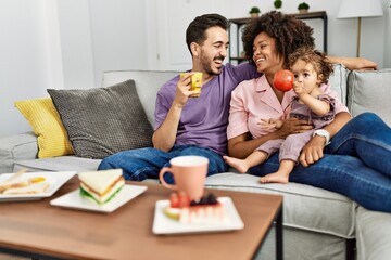 Couple and daughter having breakfast sitting on sofa at home