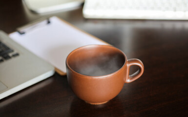 Fototapeta na wymiar brown cup with hot drink and smoke, on work desk table